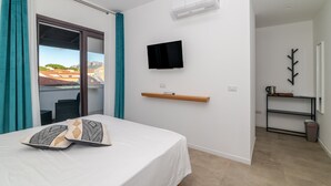 Ein Hotelzimmer mit Bett, einem an der Wand montierten Fernseher, einer kleinen Ablage und Blick nach draußen.