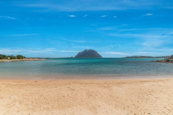 A beach with clear water, a sandy shore, and a distant mountain.