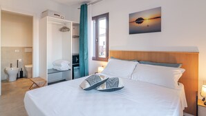 Une chambre d’hôtel avec un lit, une table de chevet, une fenêtre avec des rideaux, un tableau au mur et une salle de bain visible à travers une porte ouverte.