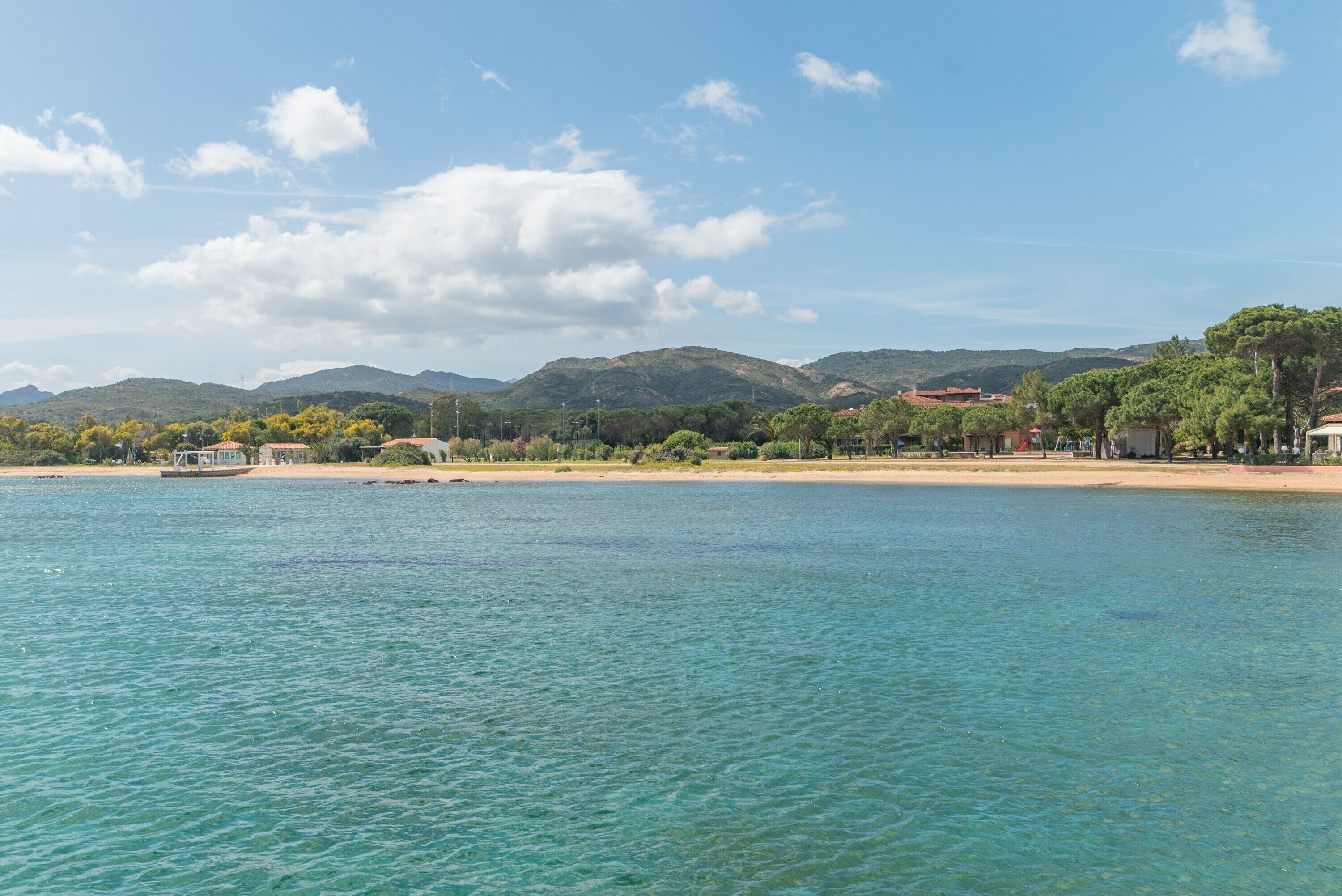 Eine Küstenlandschaft mit Strand, klarem Wasser und Bergen im Hintergrund.