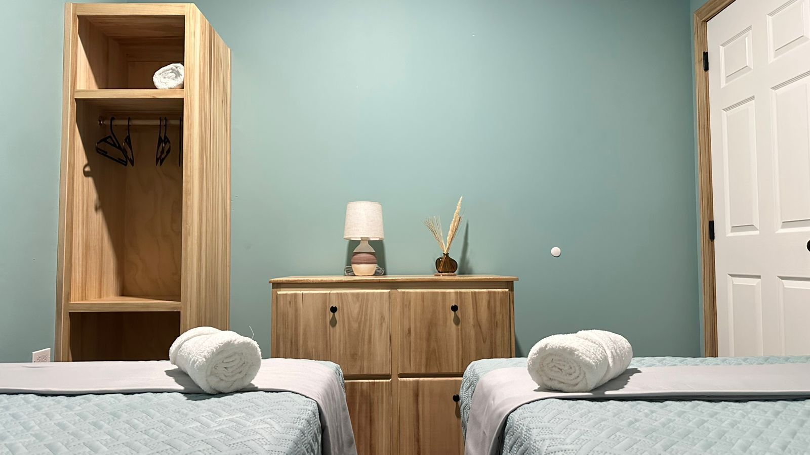 Un dormitorio con dos camas, un armario de madera, una mesita de noche con lámpara y una puerta.