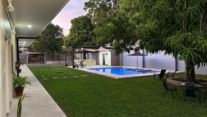 A backyard with a swimming pool, a barbecue area, and a covered seating area. - CHURROS (La Libertad)