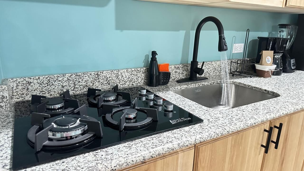 Una cocina con estufa negra, pileta de acero inoxidable y encimera de granito.