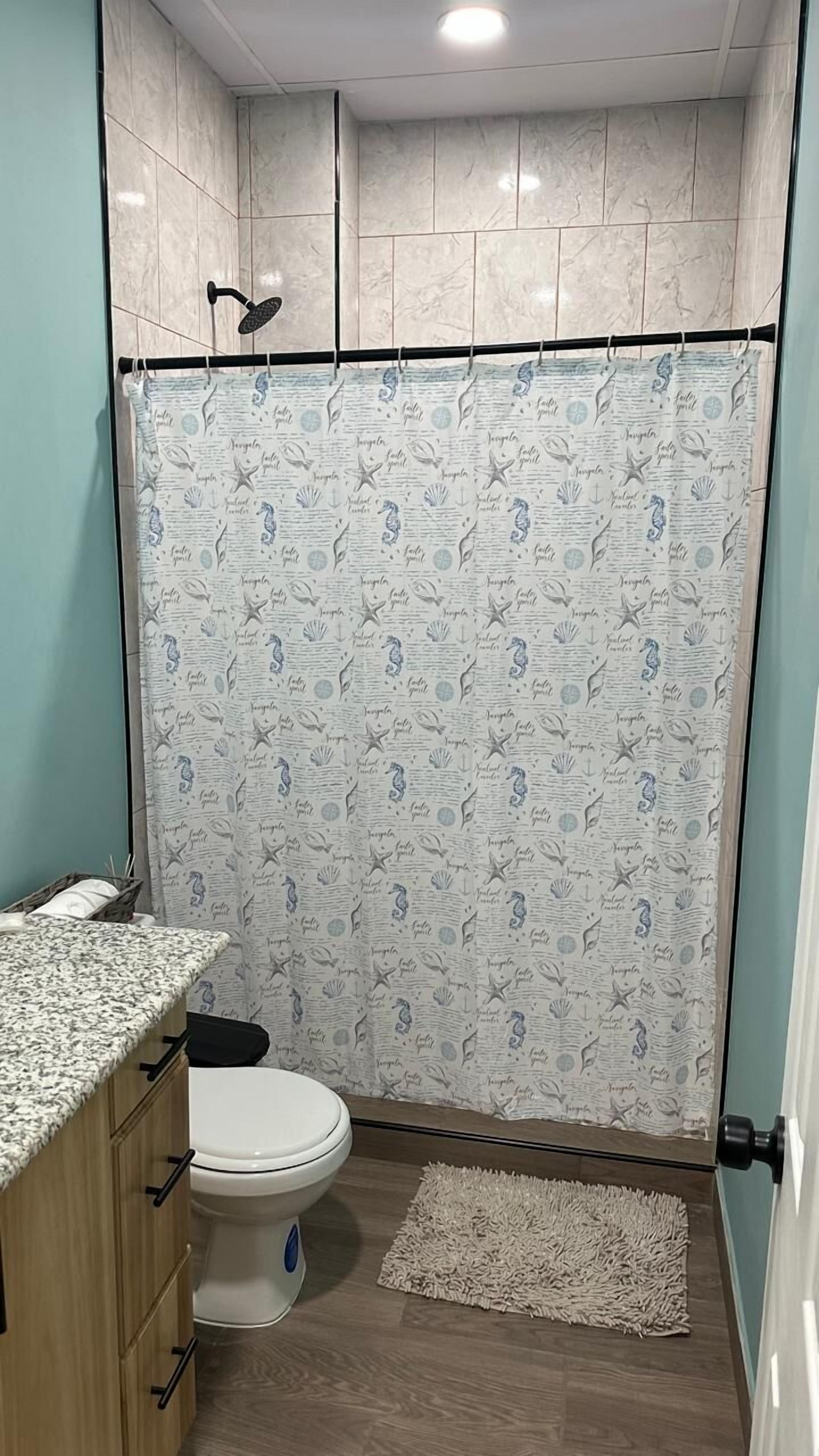 Een badkamer met een toilet, een douchegordijn met een nautisch thema, een houten kastje en een klein vloerkleed.