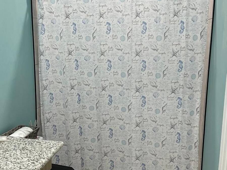 Een badkamer met een toilet, een douchegordijn met een nautisch thema, een houten kastje en een klein vloerkleed.