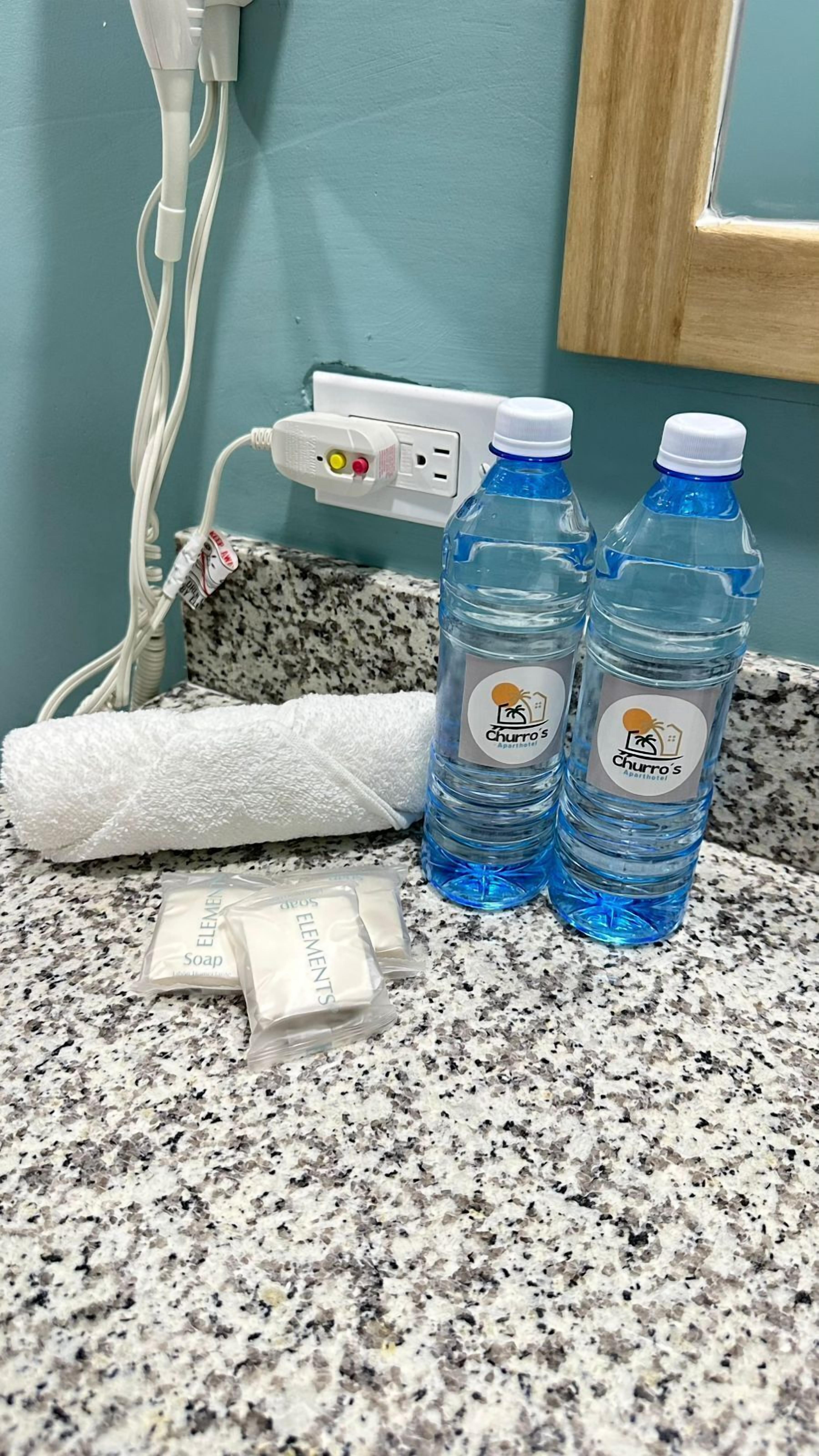 A bathroom counter with two bottles of water, a white towel, and a bag of soap.