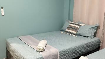 A room with two beds, each with a quilted bedspread and a rolled white towel.