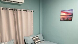 A room with two beds, a window with curtains, an air conditioning unit, and a picture on the wall. - CHURROS (La Libertad)