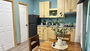 A compact kitchen with wooden cabinets, a black refrigerator, a dining table with chairs, and a vase with plants. - CHURROS (La Libertad)