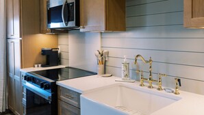 Una cocina moderna con armarios de madera, un microondas de acero inoxidable, un horno empotrado, una encimera blanca y un grifo dorado.