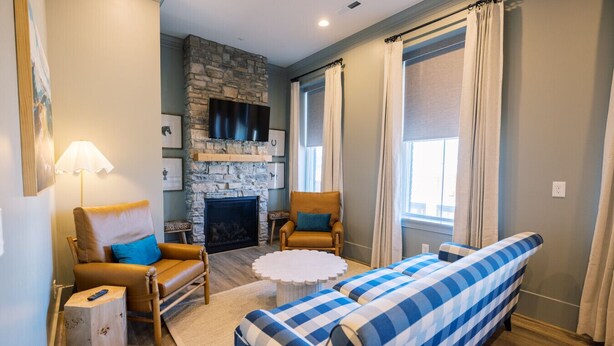 Una sala de estar acogedora con chimenea de piedra, sillones de cuero, un sofá y ventanas amplias con cortinas.