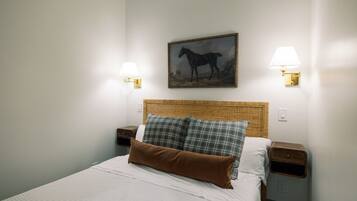 Een netjes opgemaakt bed met een witte deken en twee kussens, een rieten hoofdbord en een schilderij van een paard aan de muur.