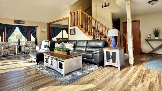 A spacious living room with a wooden staircase, leather sofa, and a ceiling fan.