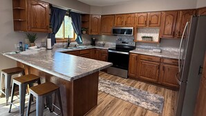 A modern kitchen with wooden cabinets, a central island with stools, a stainless steel refrigerator, and a microwave.
