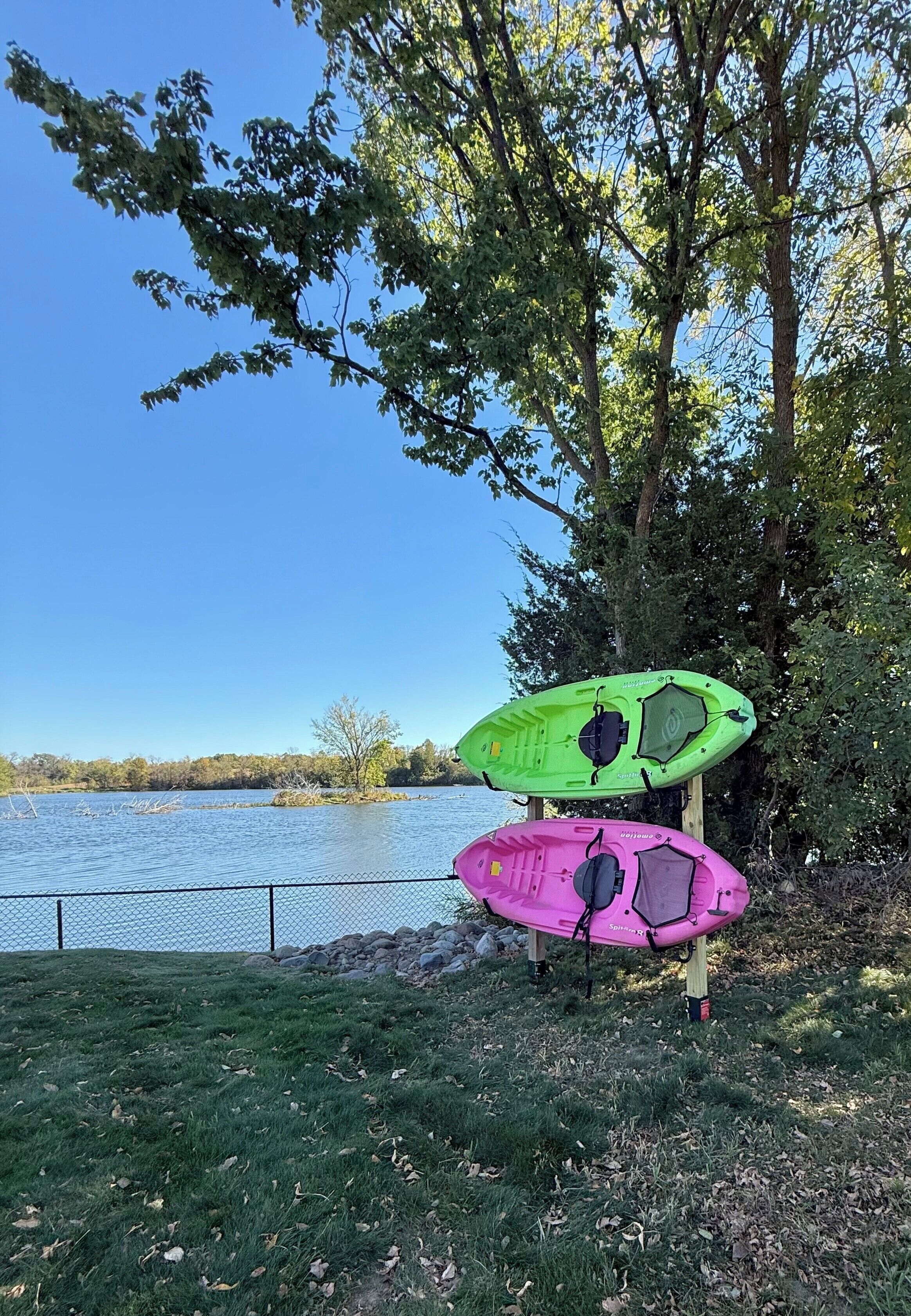 Deux kayaks sont posés sur une zone herbeuse, près d’une étendue d’eau, avec des arbres en arrière-plan.