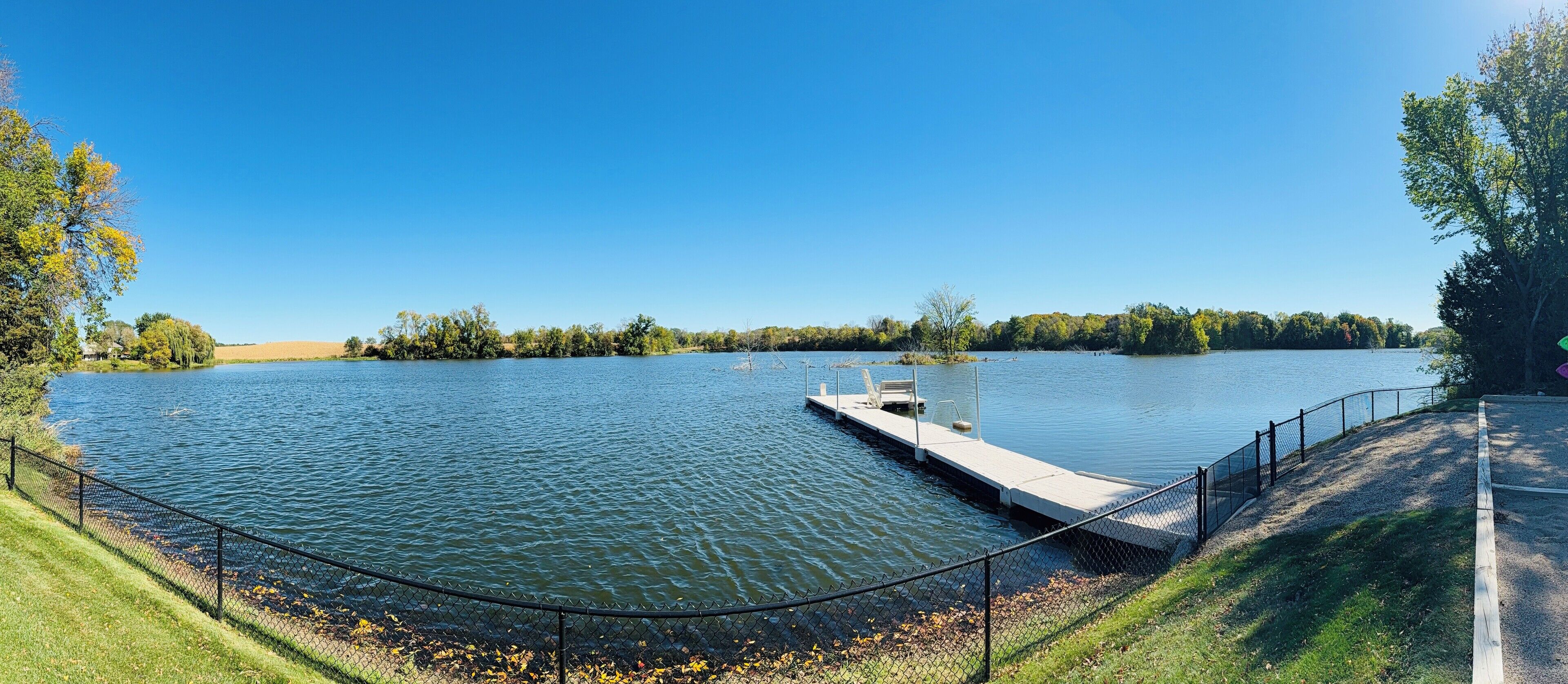 A calm lake with a dock and a fenced walkway.
