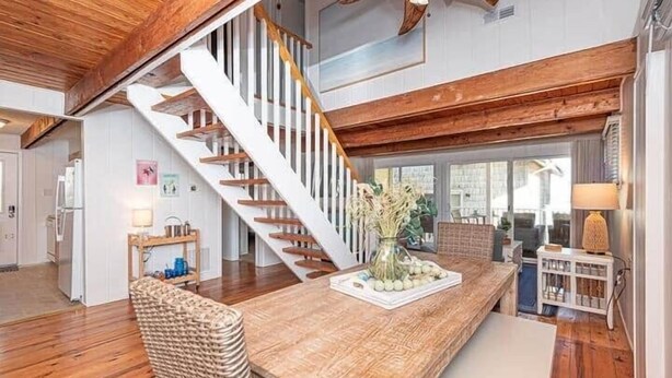 Un vaste espace de vie agrémenté d’un escalier en bois, d’une grande table en bois et offrant une vue sur l’extérieur.