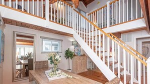 Un vaste espace dédié à la salle à manger, doté d’un plafond haut, d’un escalier en bois et offrant une vue sur la pièce adjacente.