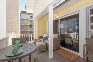 Un espace extérieur abrité, aménagé avec des meubles en osier, une table avec de la vaisselle verte et une vue sur un immeuble doté de balcons.