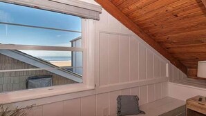 Une pièce avec un plafond en pente, une fenêtre donnant sur la plage et une petite table avec une lampe.