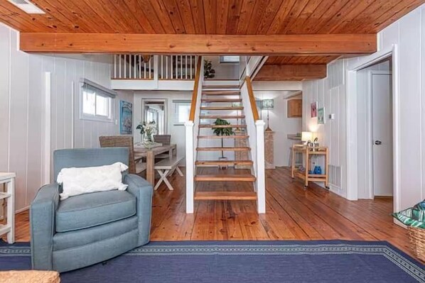 Un vaste espace de vie agrémenté d’un escalier en bois, d’un fauteuil bleu et d’une table à manger.