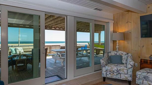 Habitación con vista al océano, una terraza de madera y un área de descanso con un sillón y reposapiés estampados.