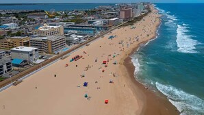 Un paisaje urbano costero con una amplia playa de arena, numerosas sombrillas y una variedad de edificios, incluyendo hoteles y residencias.