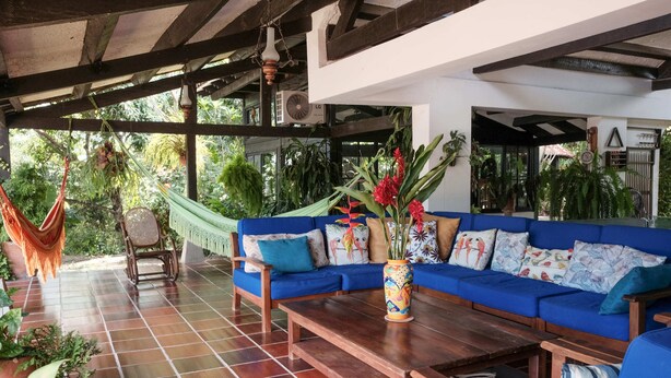 Eine überdachte Terrasse mit einem blauen Sofa, einem Holztisch und einer Hängematte.
