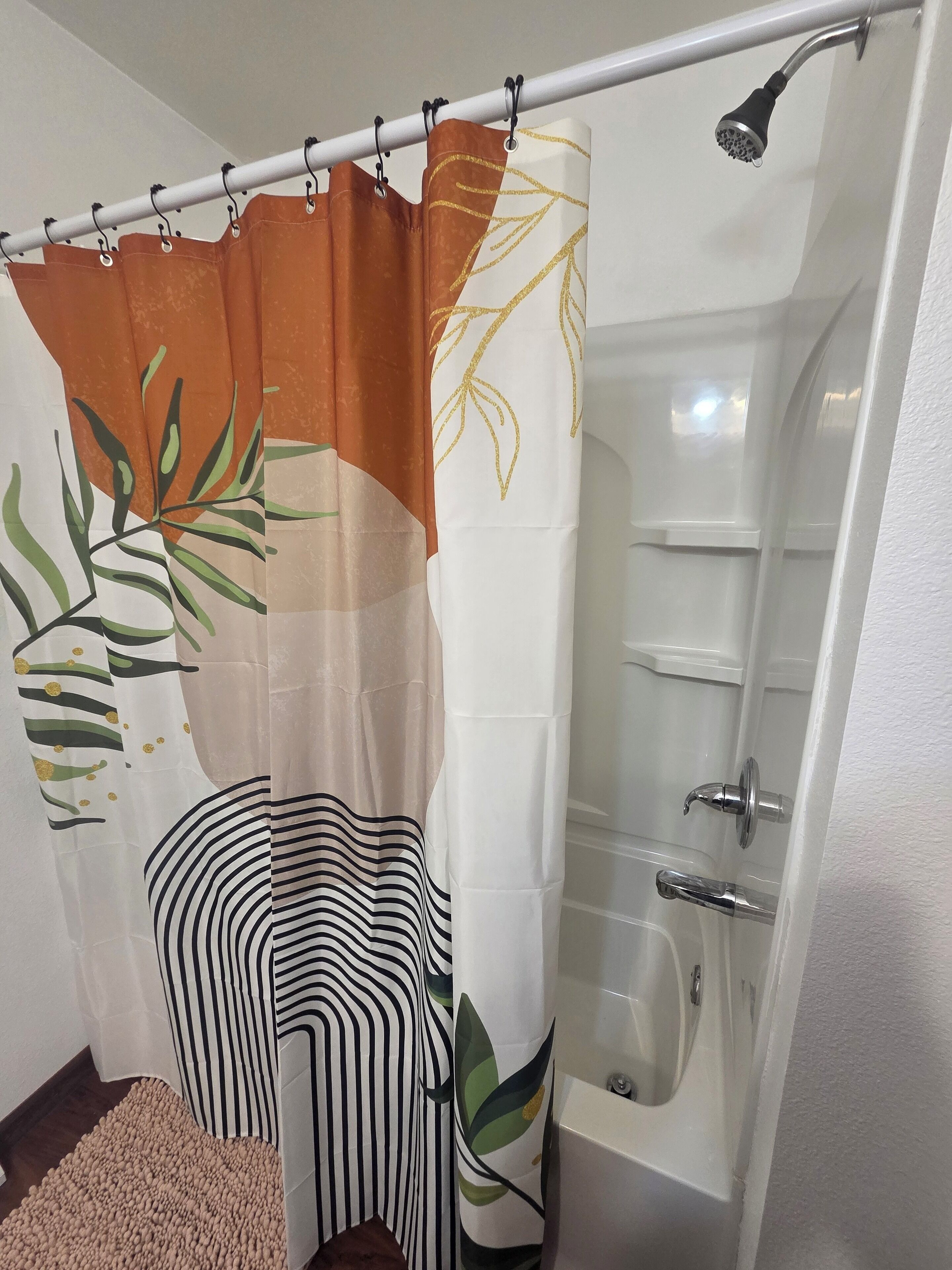 Un baño con cortina de ducha estampada con hojas, una bañera y una toalla rayada en el suelo.
