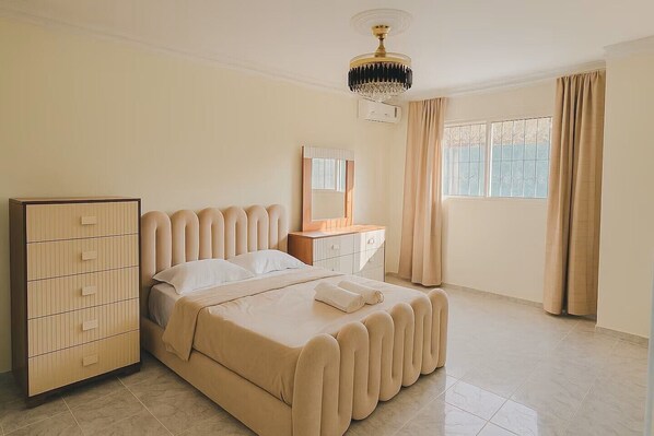 A bedroom with a bed, a dresser, a vanity, a chandelier, and a window with curtains. - Casa Moderna en la mejor zona de BONAO (Bonao)