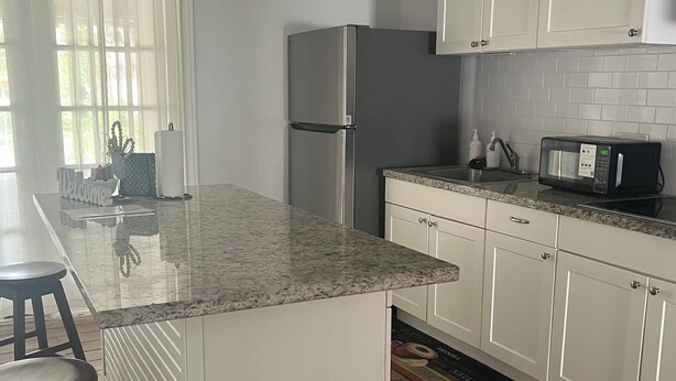 Una cocina moderna con armarios blancos, un refrigerador de acero inoxidable, un microondas y una encimera de granito.