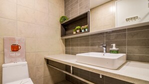 A modern bathroom with a white toilet, a white sink with a soap dispenser, and a shelf above the sink holding small potted plants. - The Robertson Residence KL (Kuala Lumpur)