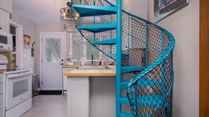 Una cocina con electrodomésticos blancos, una escalera espiral turquesa y un comedor con mesa y sillas blancas.