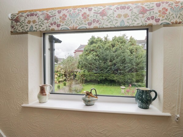 Ein Fenster mit Blick auf einen Garten und ein Gebäude. Auf der Fensterbank stehen zwei kleine Vasen.