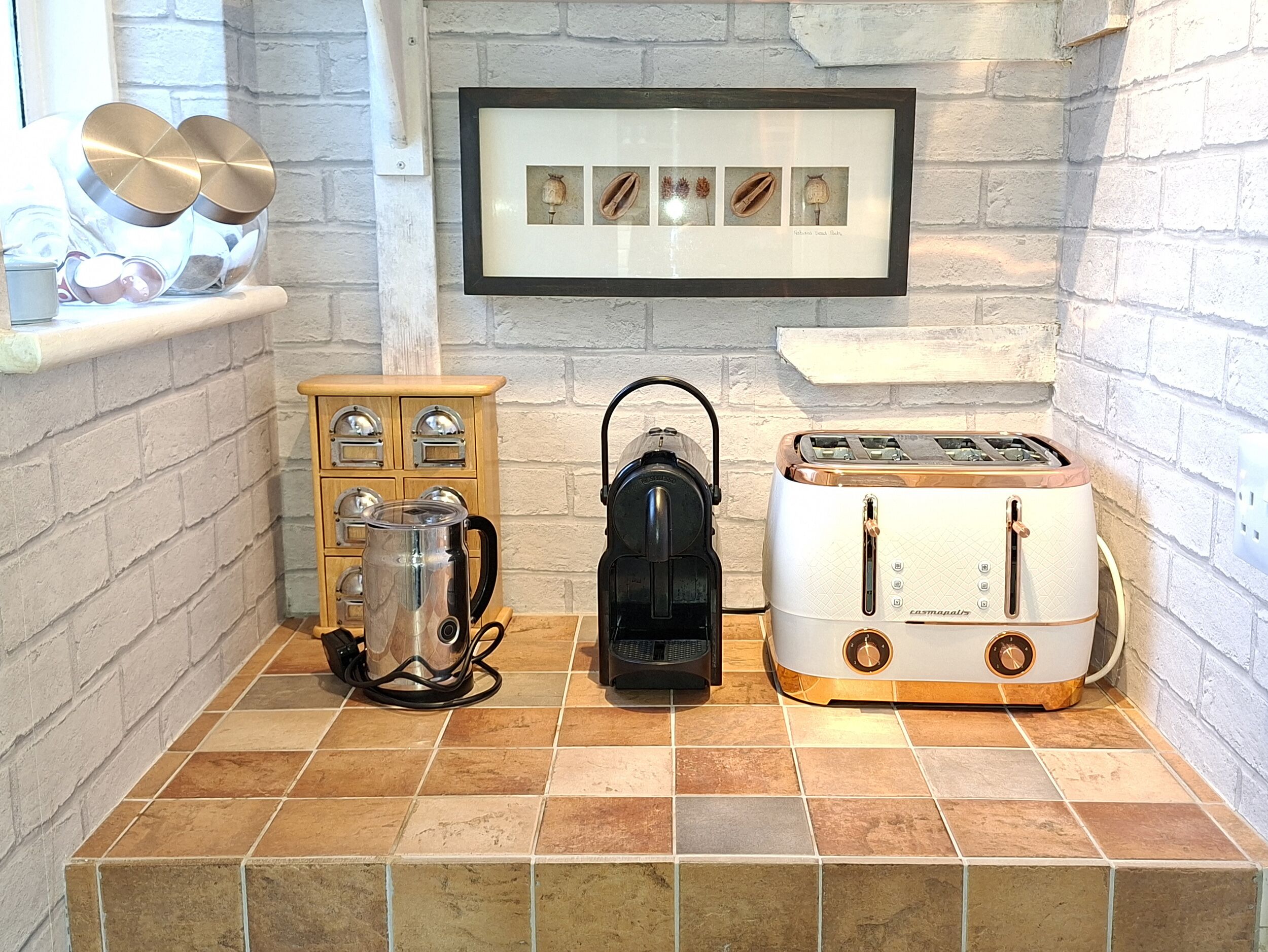 A kitchen with a coffee maker, toaster, and framed botanical prints on the wall.
