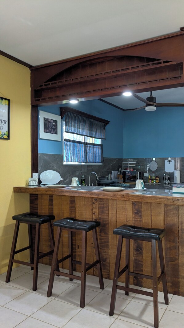 A kitchen with wooden bar stools, a marble countertop, and a window with blue curtains.