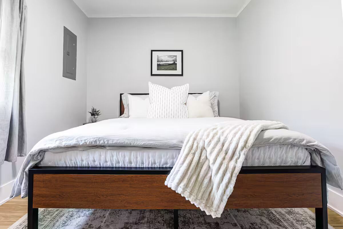 Un dormitorio con una cama, un cuadro en la pared y una ventana con cortinas.