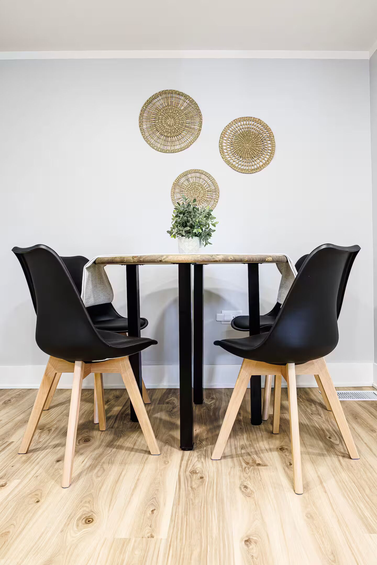 Un comedor con una mesa de madera y sillas negras, una planta pequeña sobre la mesa y tres adornos de pared tejidos.