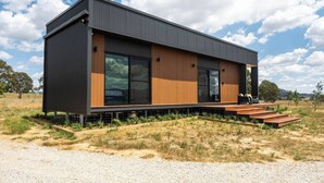 Uma casa moderna de dois andares, com janelas amplas, deck de madeira e entrada por um caminho de brita.