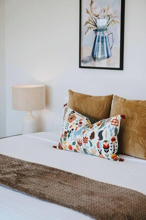 A neatly made bed with a patterned pillow and a decorative painting above it.