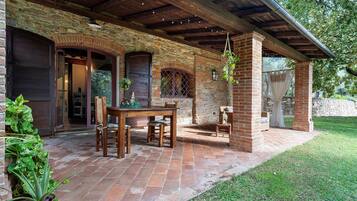 Eine überdachte Terrasse mit Backsteinwand, Holzbalkendecke und einem Tisch mit Stühlen.