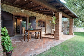 A covered patio with a brick wall, wooden ceiling beams, and a table with chairs. - Studio Apartment 'Il Nido Di Delia' with Shared Pool, Private Terrace and Wi-Fi (Buti)