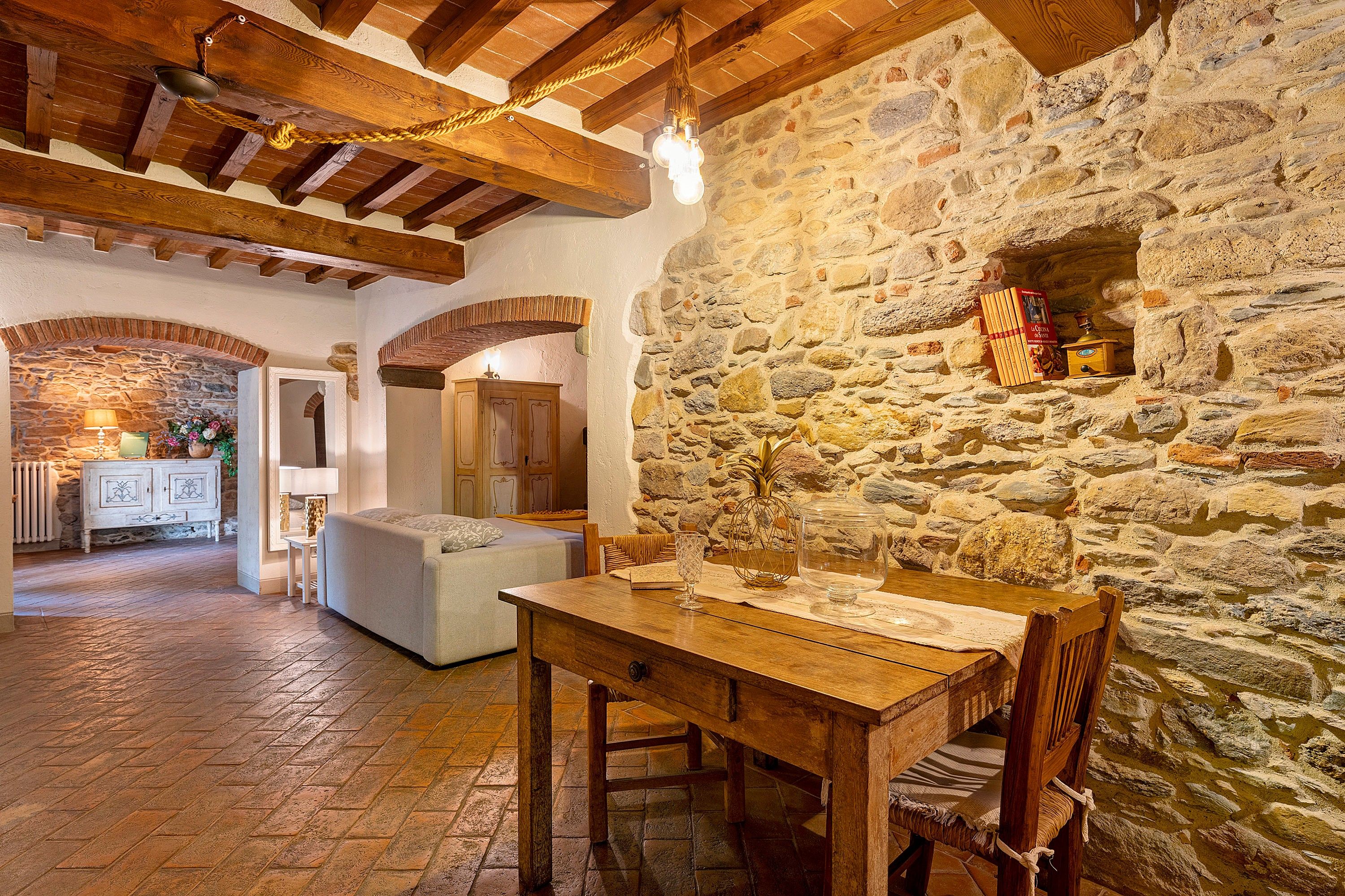 A rustic interior with exposed stone walls, wooden beams, a dining table, and a cozy seating area.