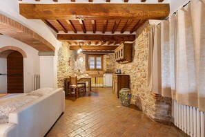 A rustic interior with exposed wooden beams, stone walls, a stone fireplace, a dining area, and a bed. - Studio Apartment 'Il Nido Di Delia' with Shared Pool, Private Terrace and Wi-Fi (Buti)