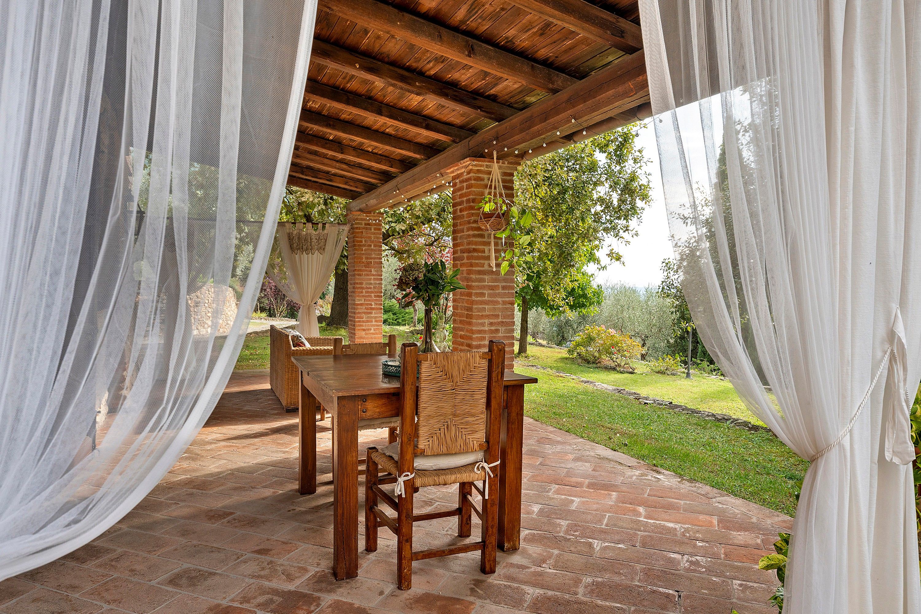 An outdoor patio with a wooden table and chairs, surrounded by white curtains.