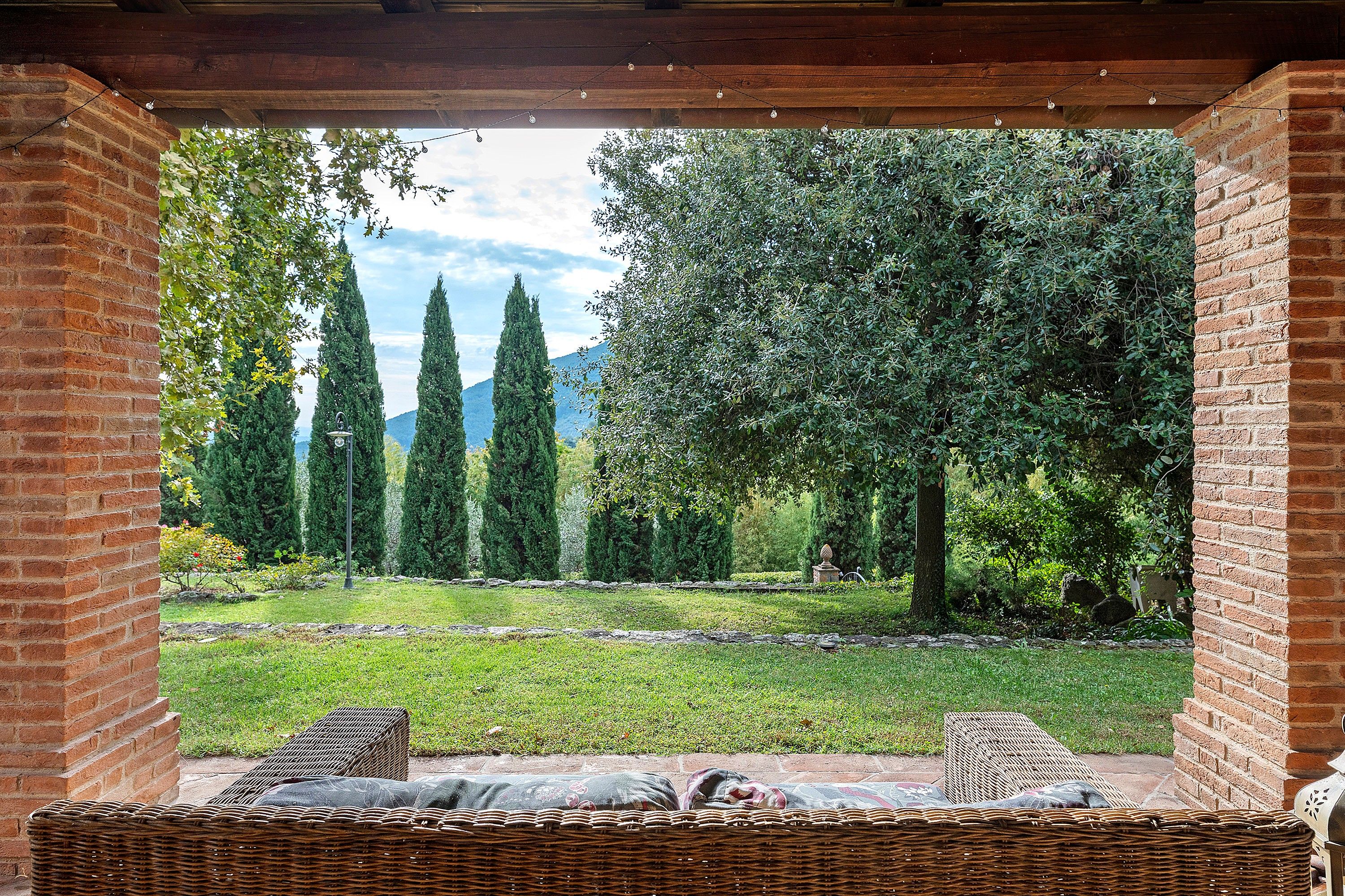 A covered outdoor seating area with a view of a garden and trees.