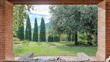A covered outdoor seating area with a view of a garden and trees.