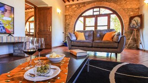 A cozy living room with a stone wall, a sofa with cushions, a television, and a dining area with a table set for two. - Villa Pierotta by MMega (Scarlino)