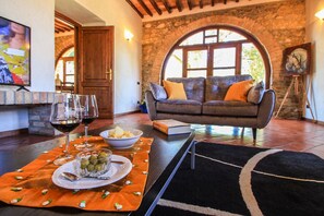 A cozy living room with a stone wall, a sofa with cushions, a television, and a dining area with a table set for two. - Villa Pierotta by MMega (Scarlino)