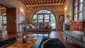 A cozy living room with a stone wall, a large arched window, and a fireplace. - Villa Pierotta by MMega (Scarlino)